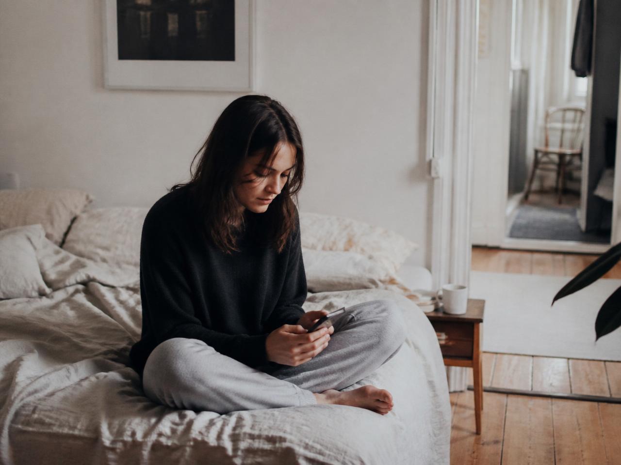 A woman sitting on her bed in soft morning light, talking through her night