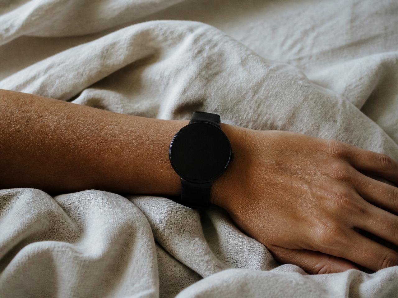 A wrist wearing a smart watch resting on soft linen in daylight